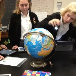 Two female students shine a flashlight at a globe. These students are observing wear the light can be seen on the global and how the movement of the earth changes this light. 